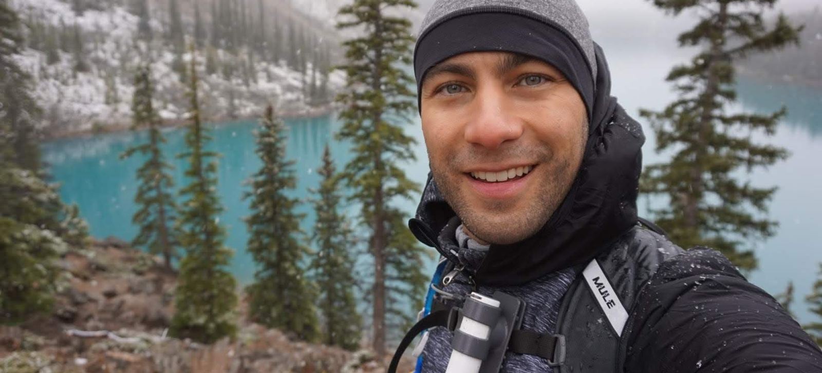 Manny taking a selfie beside a turquoise mountain lake in light snow