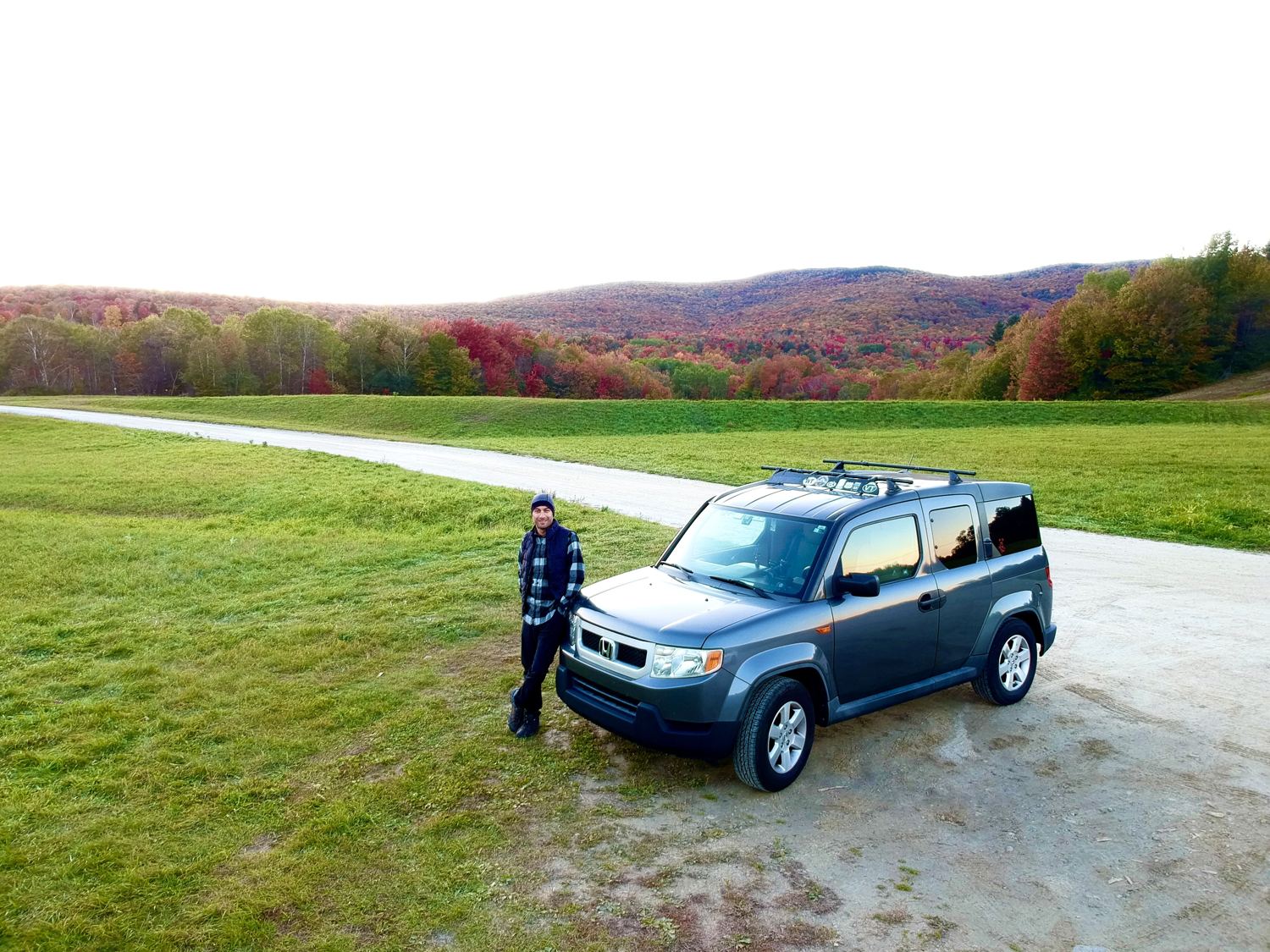 Manny leaning on a grey Honda Element below hills in autumn colours