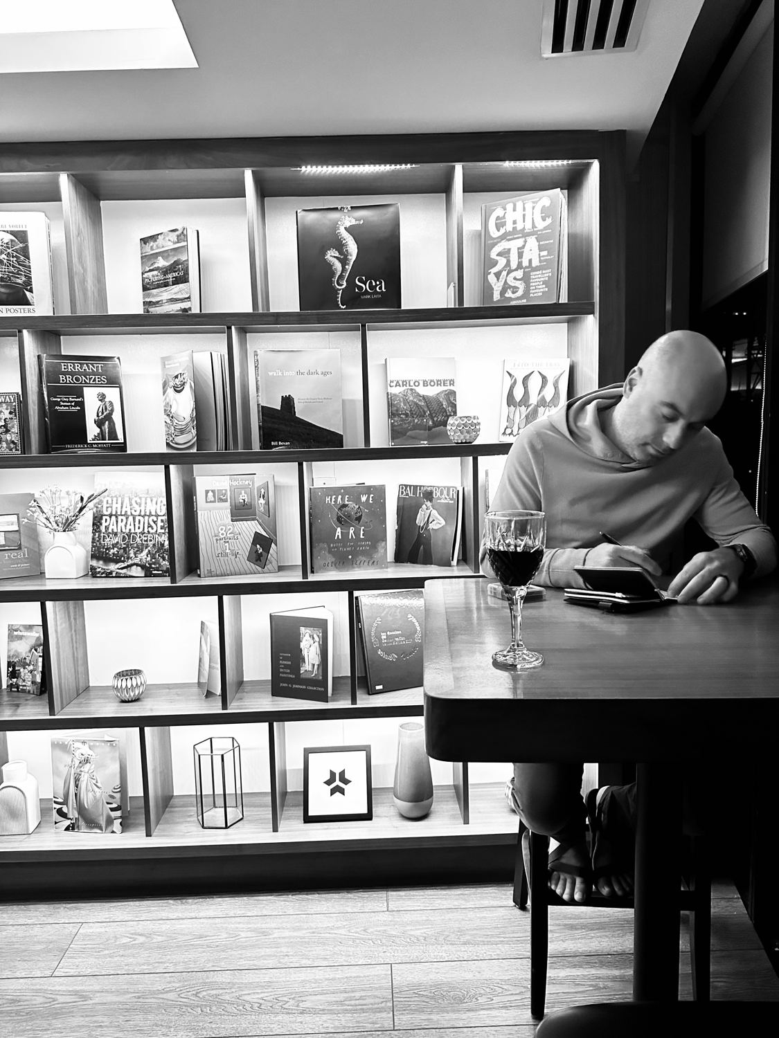 Black-and-white photo of Manny writing in a notebook beside a glass of red wine