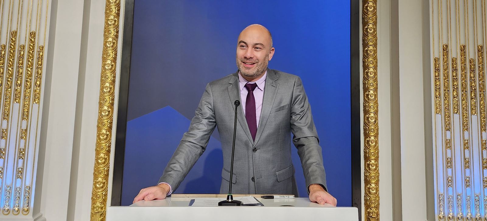 Manny speaking at an NYSE podium in front of a blue screen