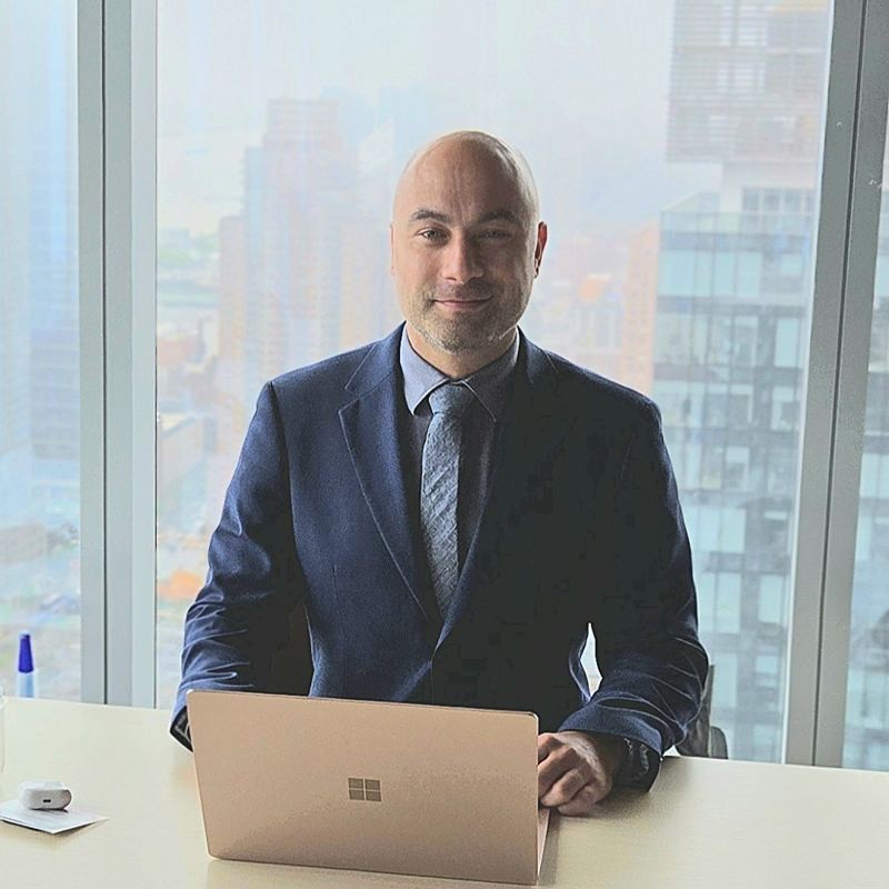 Manny at a desk in front of a high-rise window